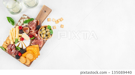 Antipasto board with assorted cheeses, cured meats, crackers, figs, olives, berries, and fresh herbs on a wooden serving board, top view, copy space 135089440