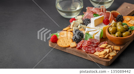 Assorted antipasto board with cheese, cured meats, olives, crackers, figs, and berries on a wooden serving board, dark background, top view 135089442