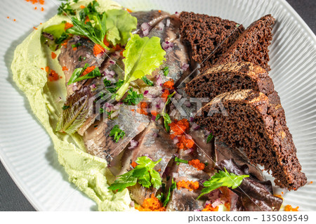 Marinated herring with rye bread, herbs, and red onion on a white plate 135089549