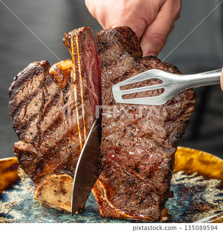 Juicy porterhouse steak being sliced in chefs hands 135089594