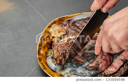 Chef slicing juicy porterhouse steak on a plate. top view. copy space Chef slicing juicy porterhouse steak on a plate. top view. copy space 135089596