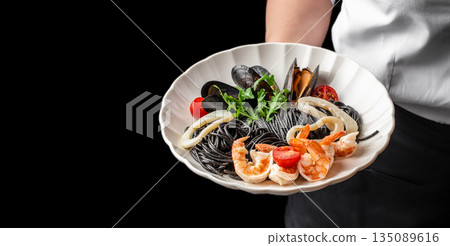chef hands with Black spaghetti with seafood served on a white plate in hand. copy space chef hands with Black spaghetti with seafood served on a white plate in hand. copy space 135089616