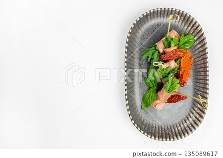Prosciutto rolls with arugula and sun-dried tomatoes on a stylish dark plate. top view. copy space Prosciutto rolls with arugula and sun-dried tomatoes on a stylish dark plate. top view. copy space 135089617