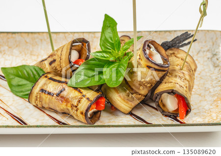 Grilled eggplant rolls with cheese and red pepper on a ceramic plate 135089620
