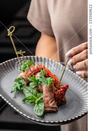 Prosciutto rolls with arugula and sun-dried tomatoes served in hand 135089622