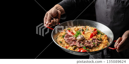 chef hands with Paella with beef, peppers and garlic served in a pan. copy space chef hands with Paella with beef, peppers and garlic served in a pan. copy space 135089624