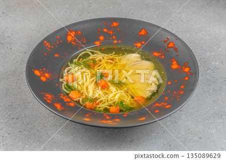 Traditional chicken noodle soup with tender meat, julienned carrots, and fresh dill served in a decorative black bowl Traditional chicken noodle soup with tender meat, julienned carrots, and fresh dill served in a decorative black bowl 135089629