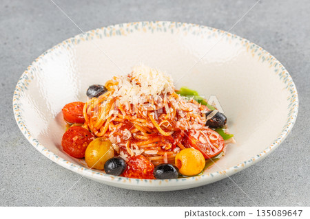 A vibrant plate of spaghetti with tomato sauce is topped with grated cheese, cherry tomatoes, black olives, and yellow cherry peppers 135089647