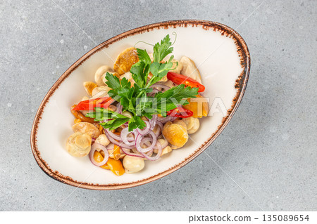 A marinated mushroom salad served with red onion rings, slices of red chili pepper, and fresh parsley on a rustic ceramic plate 135089654