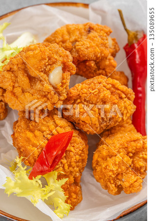 Crispy golden fried chicken pieces served on parchment paper with red chili pepper and fresh lettuce garnish 135089655