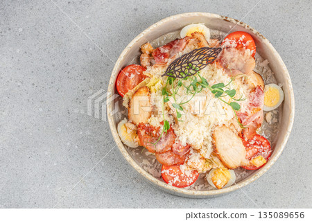 Fresh Caesar salad with grilled chicken breast, cherry tomatoes, crispy bacon, grated cheese, croutons, and quail eggs on a rustic ceramic plate. top view. copy space 135089656