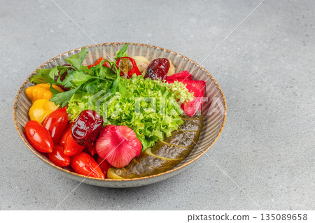 Assorted pickled vegetables including cucumbers, peppers, cabbage, onions, and fresh lettuce garnished with parsley in a rustic bowl Assorted pickled vegetables including cucumbers, peppers, cabbage, onions, and fresh lettuce garnished with parsley in a rustic bowl 135089658