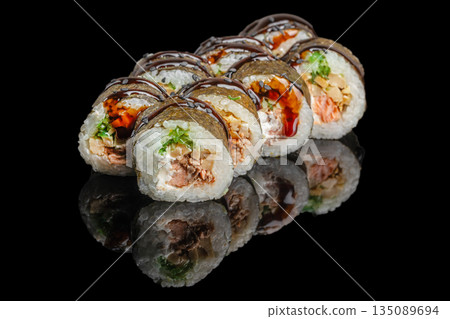 Sushi rolls filled with salmon, cream cheese, greens, and vegetables are topped with dark sauce and elegantly displayed on a black reflective surface 135089694