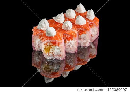 Bright sushi rolls wrapped in pink soy paper and topped with fresh salmon and dollops of cream cheese are filled with rice, crab, tobiko, and sliced yellow vegetables, on a reflective black surface 135089697
