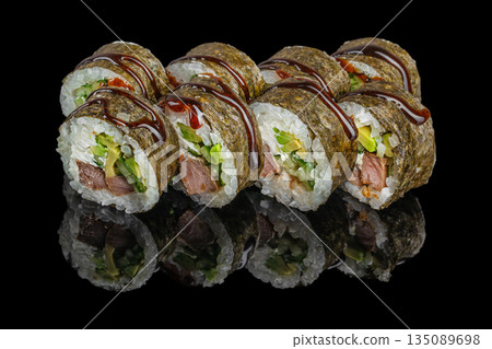 Sushi rolls wrapped in nori and filled with rice, avocado, cucumber, cream cheese, and cooked meat are drizzled with dark teriyaki sauce and displayed on a reflective black surface 135089698