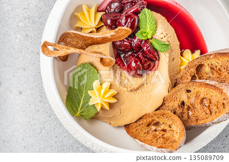 Creamy pate is elegantly served with cherry compote, toasted baguette slices, whipped butter, and fresh mint for a refined appetizer 135089709