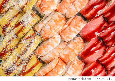 A vibrant assortment of sushi rolls features shrimp, tuna, and egg-topped varieties, garnished with sauces and grated cheese for an eye-catching gourmet presentation A vibrant assortment of sushi rolls features shrimp, tuna, and egg-topped varieties, garnished with sauces and grated cheese for an eye-catching gourmet presentation 135089719
