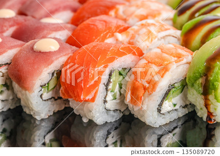 An assorted sushi platter showcases vibrant rolls topped with tuna, salmon, shrimp, and avocado, reflecting freshness, variety, and culinary artistry An assorted sushi platter showcases vibrant rolls topped with tuna, salmon, shrimp, and avocado, reflecting freshness, variety, and culinary artistry 135089720