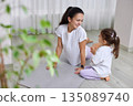 Mother and daughter bonding through home yoga practice on a mat 135089740