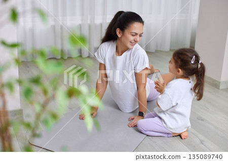 Mother and daughter bonding through home yoga practice on a mat 135089740