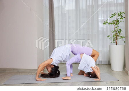 Mother and daughter exercising in a bridge pose on a mat at home Mother and daughter exercising in a bridge pose on a mat at home 135089766