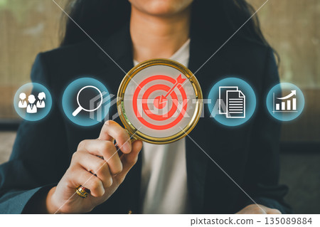 Businesswoman using magnifying glass with target icon, symbolizing focus on business strategy, goals, and success. 135089884