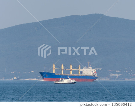 August 12, 2025: Cargo ship Yeditepe entering the port of Novorossiysk, Russia, with mountains in the background 135090412