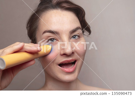Close up of Caucasian attractive woman using microcurrent facial toning device at home. Beauty popular device with LED 135090473