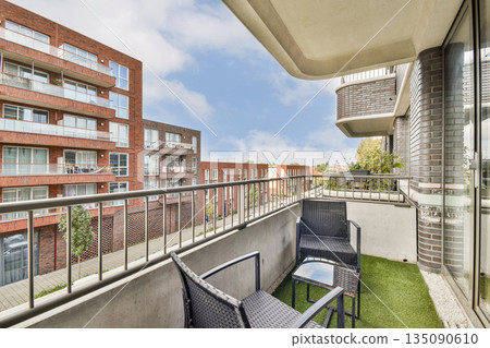 A stylish balcony features outdoor seating and a view of modern apartment buildings, creating a contemporary urban atmosphere. Ideal for relaxation. A stylish balcony features outdoor seating and a view of modern apartment buildings, creating a contemporary urban atmosphere. Ideal for relaxation. 135090610