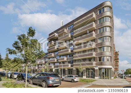 A contemporary multi-story building featuring a unique design, surrounded by trees and parked cars, showcasing urban architecture and landscape integration. A contemporary multi-story building featuring a unique design, surrounded by trees and parked cars, showcasing urban architecture and landscape integration. 135090619