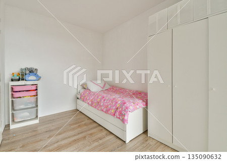 A minimalist child's bedroom featuring light walls, a single bed with colorful bedding, and simple storage solutions for toys and essentials. 135090632