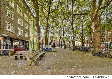 A picturesque urban park scene featuring benches, shaded trees, and cafe seating, perfect for relaxation and social gatherings in the heart of the city. 135090674