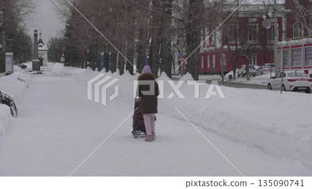 28 December 2025, Barnaul, Russia. Woman with child walks along the central park alley in winter, enjoying sledding, snowy landscape, and urban outdoor recreation. 135090741