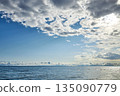 Blue sky with fluffy white and grey clouds over a vast, calm body of water 135090779