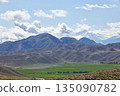 Vast mountain landscape with a green valley and distant snow-capped peaks 135090782