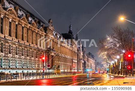 Louvre Museum stands in Paris, France. Winter night scene features the historic palace facade along Quai Francois Mitterrand with red traffic lights reflecting on wet snow Louvre Museum stands in Paris, France. Winter night scene features the historic palace facade along Quai Francois Mitterrand with red traffic lights reflecting on wet snow 135090986