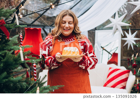 Lemon, vanilla marble bund cake in woman hands. Happy 30s girl standing near decorated Christmas tree. Winter time and holidays. Celebration banner, Lemon, vanilla marble bund cake in woman hands. Happy 30s girl standing near decorated Christmas tree. Winter time and holidays. Celebration banner, 135091026