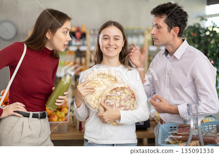 Teenage girl holding pizza while parents disagree in grocery Teenage girl holding pizza while parents disagree in grocery 135091338