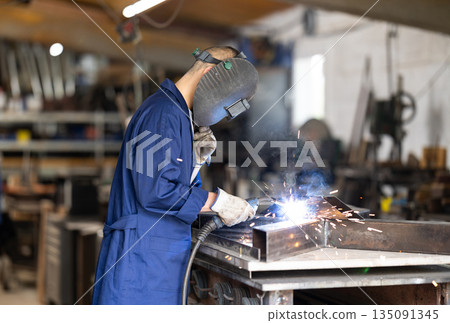 Male welder standing with a welding semi-automatic machine and a safety helmet in metal machining workshop 135091345