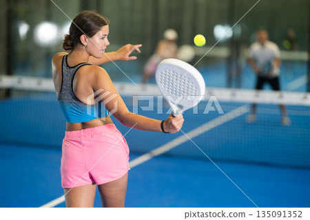 Young woman playing tennis against man and woman 135091352