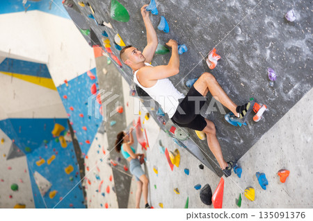 Young man climbing on artificial rock wall in rock-climbing gym 135091376