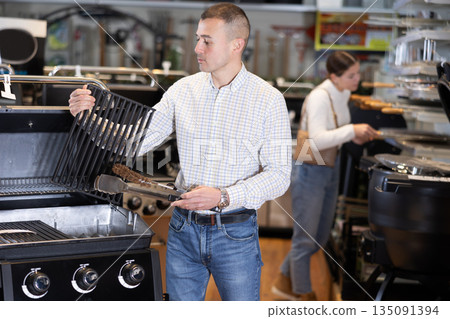 In store, man inspects mobile grill, buys barbecue device 135091394
