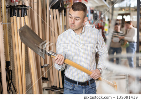 Amateur gardener man selects necessary items tools for her hobby in greenhouse flower-bed 135091419