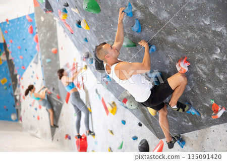 Atlete man grabbing ledges of artificial climbing wall in bouldering centre 135091420