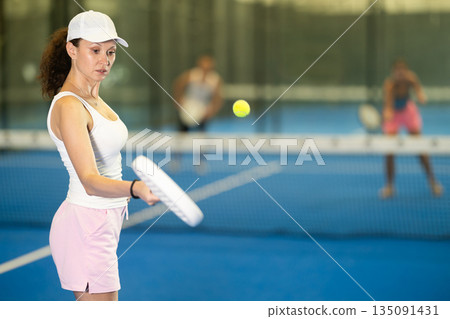 Woman playing padel on indoor court on summer day. Sport and active lifestyle concept Woman playing padel on indoor court on summer day. Sport and active lifestyle concept 135091431