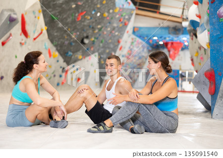 Three climbing friends sit on the floor and discuss options for climbing climbing wall. Share their impressions Three climbing friends sit on the floor and discuss options for climbing climbing wall. Share their impressions 135091540