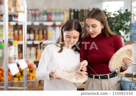 Teenage girl and her mother choosing pizza in grocery store Teenage girl and her mother choosing pizza in grocery store 135091550