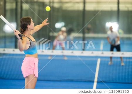 Young woman playing tennis against man and woman 135091560