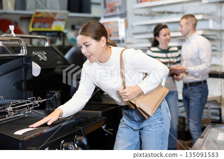 Young woman shopping at garden supermarket - choosing new grill for frying meat 135091583