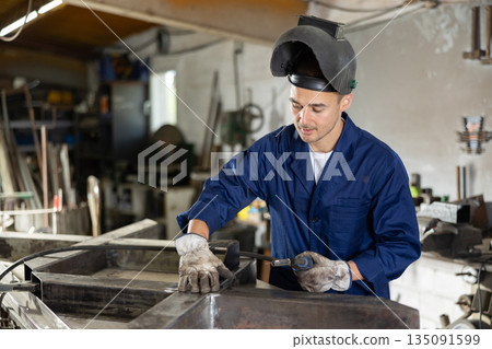 Young man welding metal part in workshop Young man welding metal part in workshop 135091599